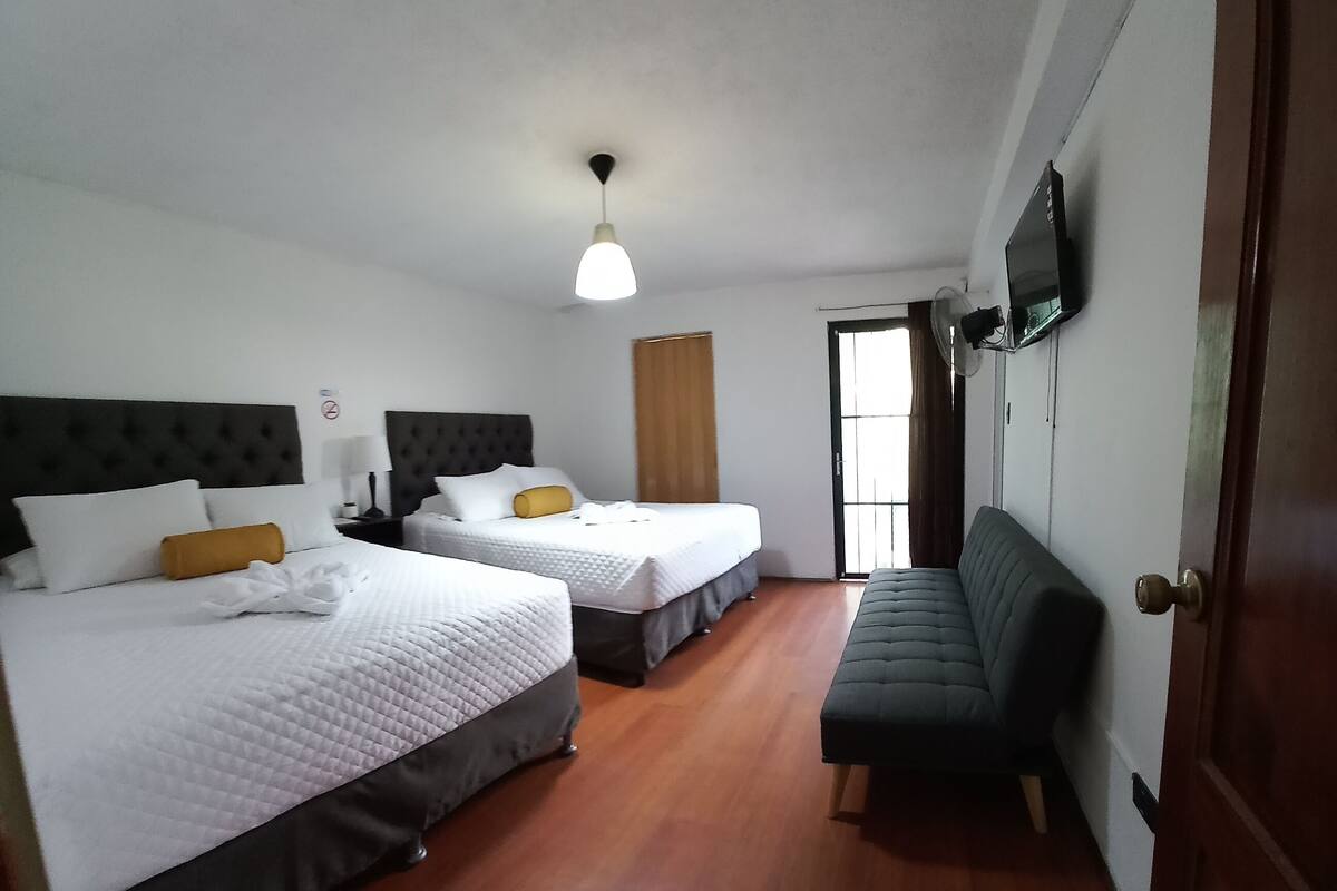 Une chambre d’hôtel avec deux lits, un canapé, une télévision et un ventilateur de plafond.