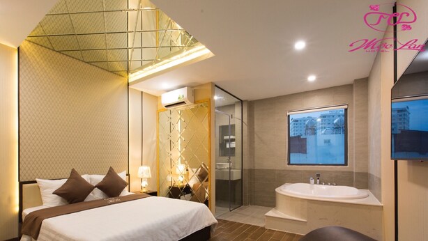 Une chambre d’hôtel moderne dotée d’un grand lit, d’une salle de bain séparée avec baignoire, d’une douche en verre et d’une grande fenêtre offrant une vue sur la ville.