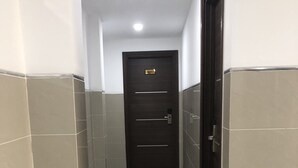 Un couloir étroit, carrelé, avec une porte sombre au fond, qui donne sur une pièce.