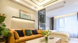 A modern hotel room with a sofa, a coffee table, a bed, a large mirror, and a window with curtains. - HO Cotel Apartment (Chengdu)
