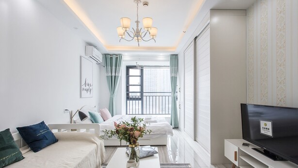 A modern living room with a sofa, coffee table, TV, and a balcony with curtains. - HO Cotel Apartment (Chengdu)