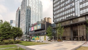 A modern building with a glass facade, a landscaped courtyard, and a parking area. - HO Cotel Apartment (Chengdu)