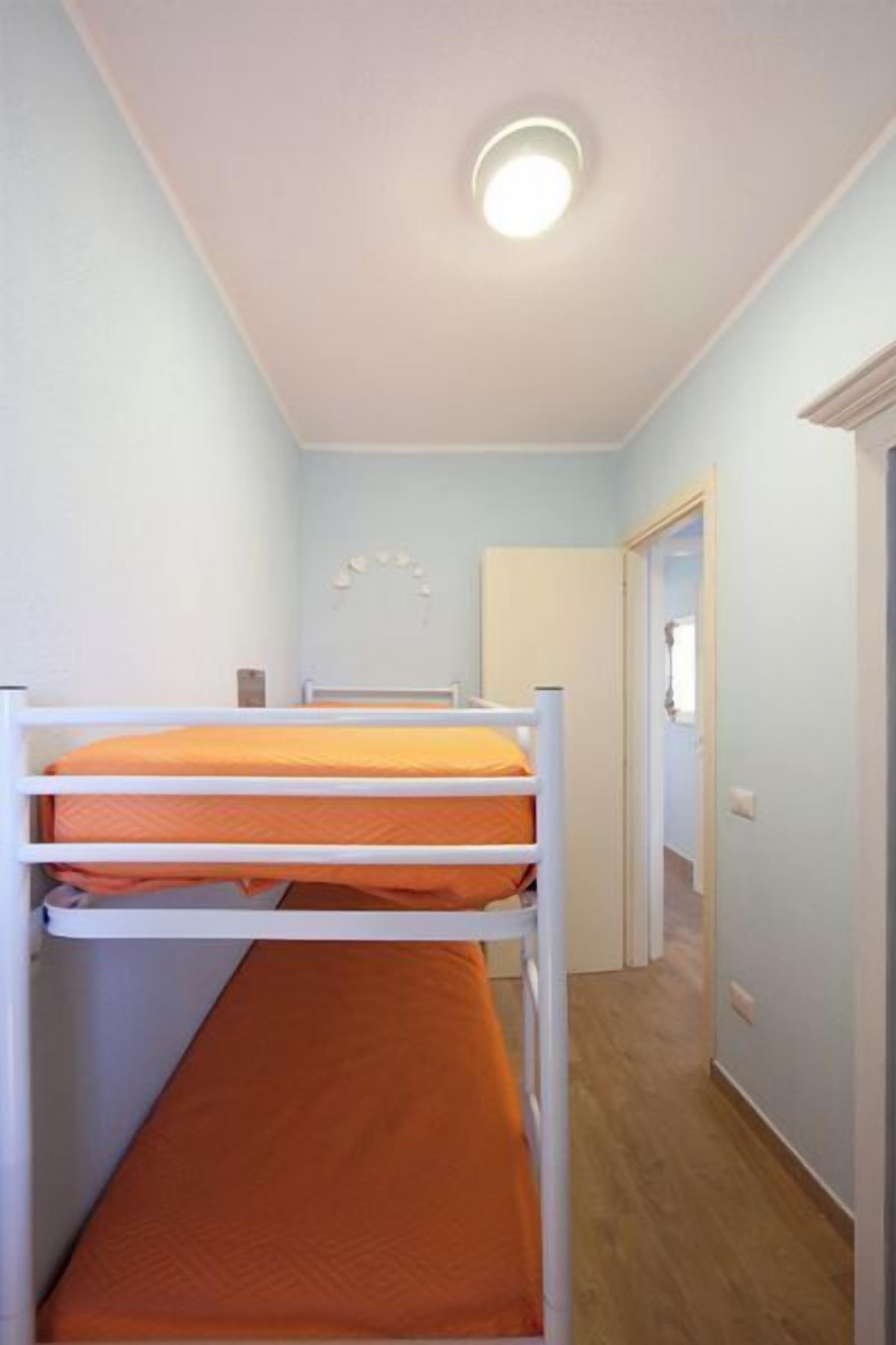 Un lit superposé avec une literie orange, dans une pièce aux murs bleu clair et au plancher en bois.
