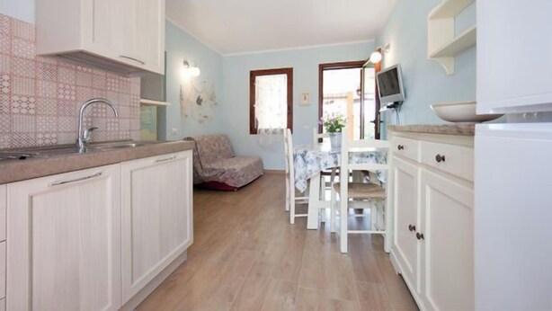 A kitchen with white cabinets, a sink, and a dining area with a table and chairs. - A beautiful villaetta overlooking the sea (COSTA REI)