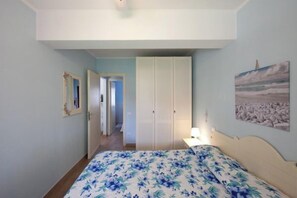 A bedroom with a bed, a wardrobe, a painting, and a hallway leading to another room.