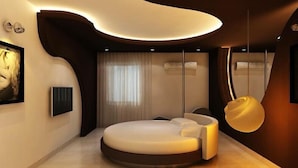 Ein modernes Schlafzimmer mit gewölbter Decke, einem großen Bett, einem wandmontierten Fernseher und einer Pendelleuchte.