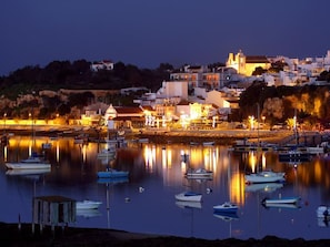 A coastal town at dusk with boats docked in calm waters, a prominent church on a hill, and buildings with warm lighting.
