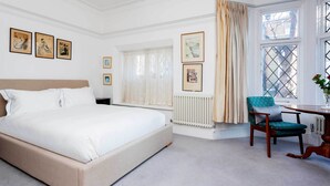 A bedroom with a large bed, a chair, a table, and a window with curtains. - Richmond on Canvas, by Veeve (London)