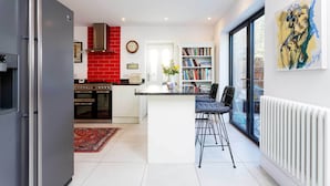 A modern kitchen with a red brick backsplash, a built-in oven, and a dining area with a white island and black bar stools. - Richmond on Canvas, by Veeve (London)