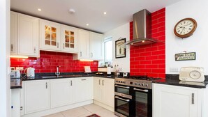 A kitchen with white cabinets, red backsplash, stainless steel appliances, and a clock on the wall. - Richmond on Canvas, by Veeve (London)