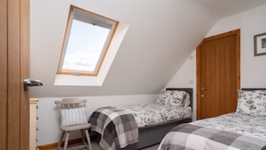 Une chambre avec un plafond en pente, un puits de lumière, un lit simple, une chaise, une armoire en bois et une porte.