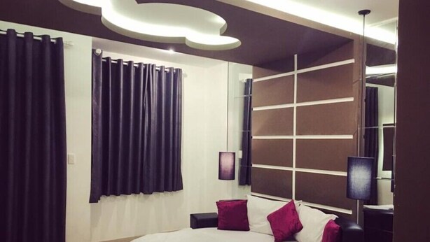 A modern bedroom with a large bed, dark curtains, a wall-mounted TV, and a bedside table. - Moc Lan 3 Hotel (Ho Chi Minh City)
