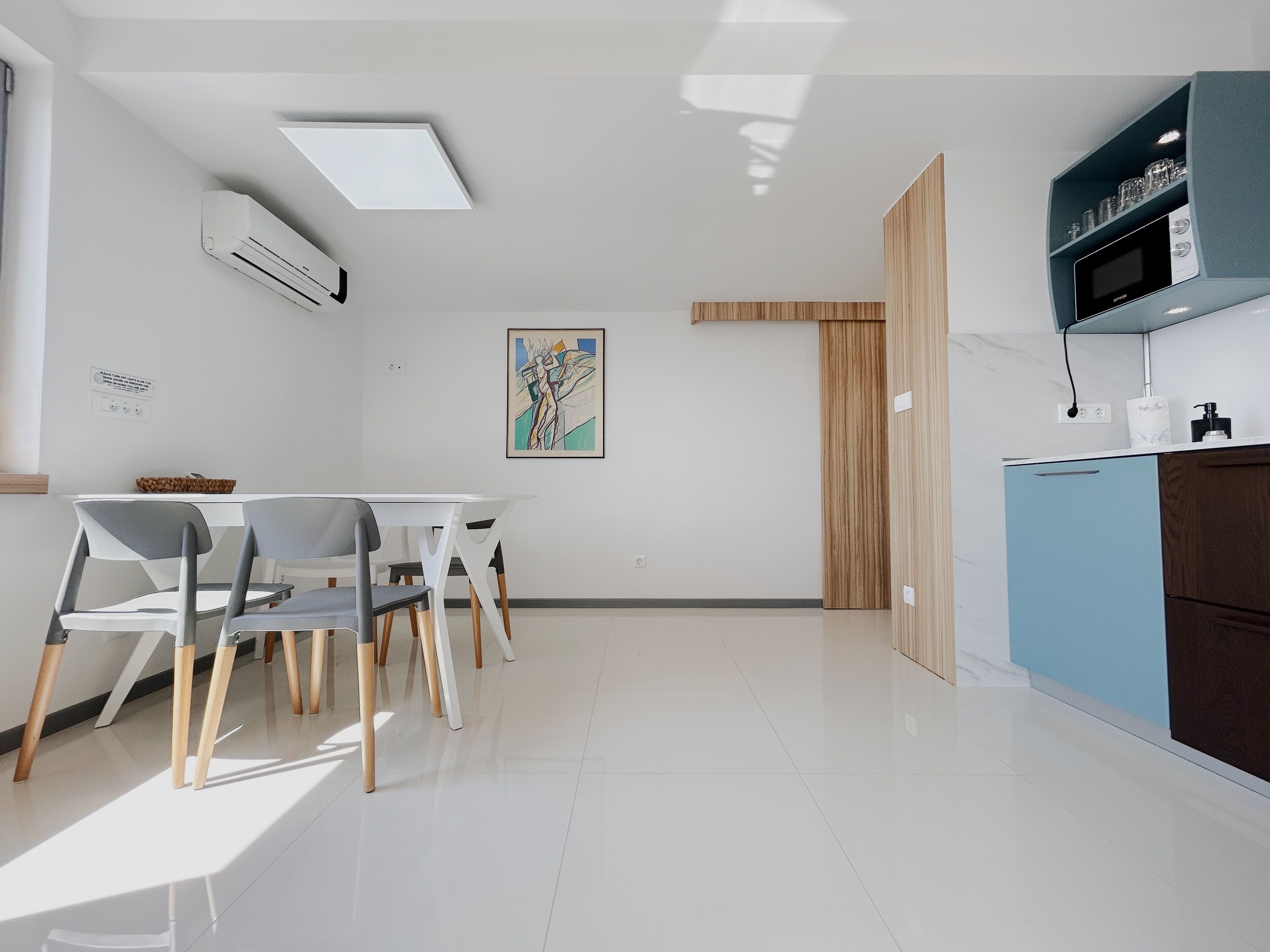 Een moderne keuken met witte kasten, een blauw aanrecht en een eethoek met een witte tafel en stoelen.