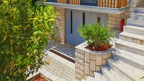 A modern two-story house with a stone facade, a wooden balcony, and a small garden area with a tree and shrubbery. - October in Luxury Sea-View Stay near Sandy Beach (Zambratija)