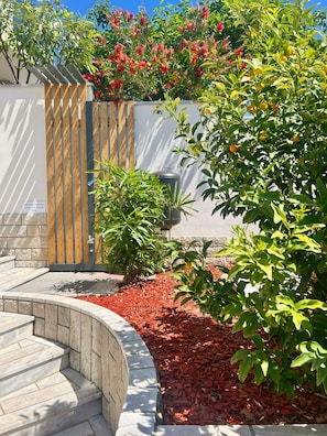 A landscaped garden with a wooden fence, a stone wall, and a variety of plants including red flowering bushes and a citrus tree. - Luxury Sea-View Stay Near Sandy Beach (Zambratija)