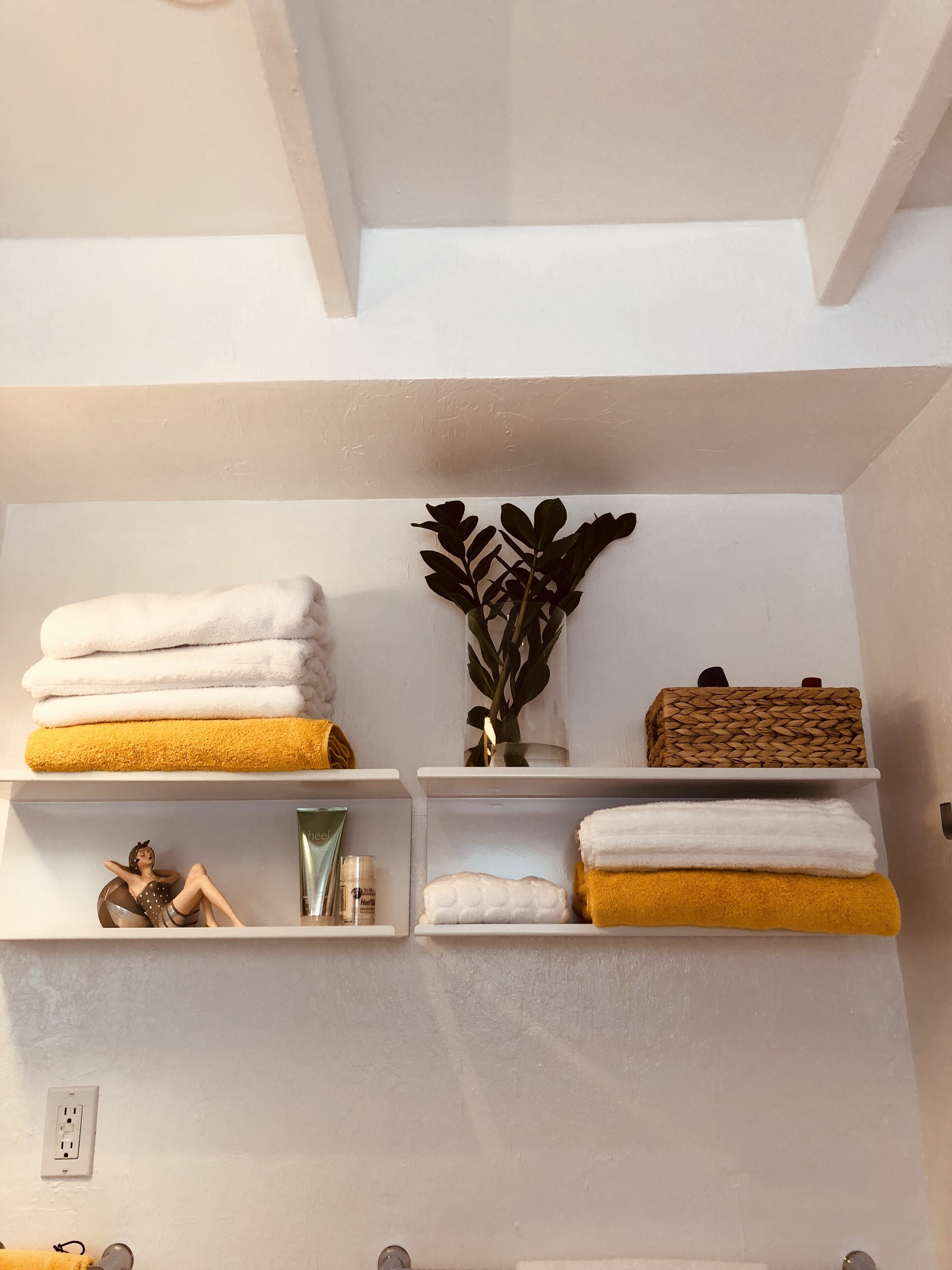 A bathroom with white shelves holding towels, a decorative plant, and toiletries.