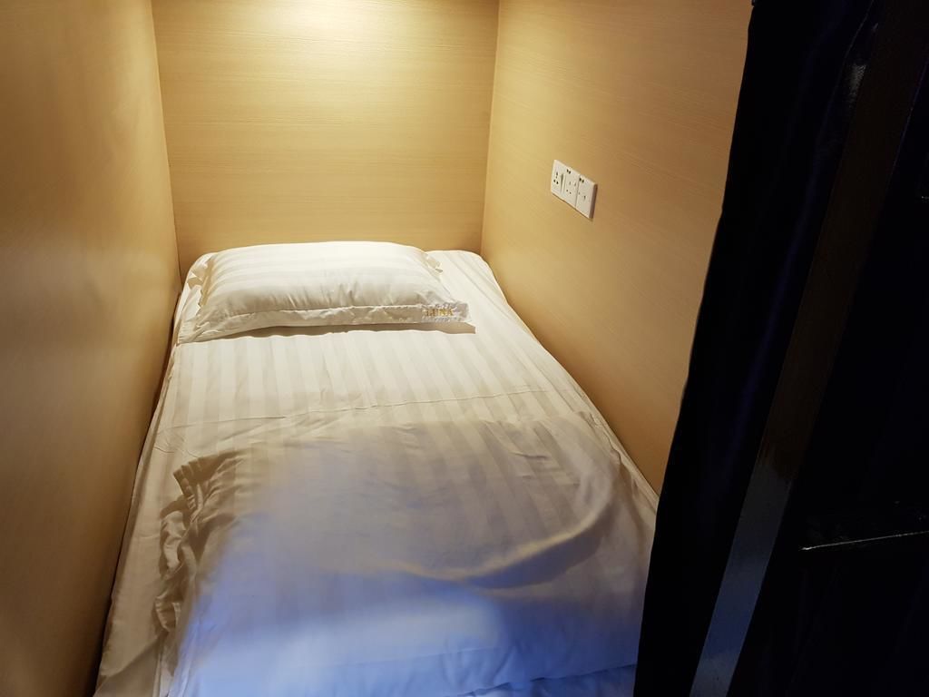 Une petite chambre avec un lit simple, un mur uni et une prise de courant.