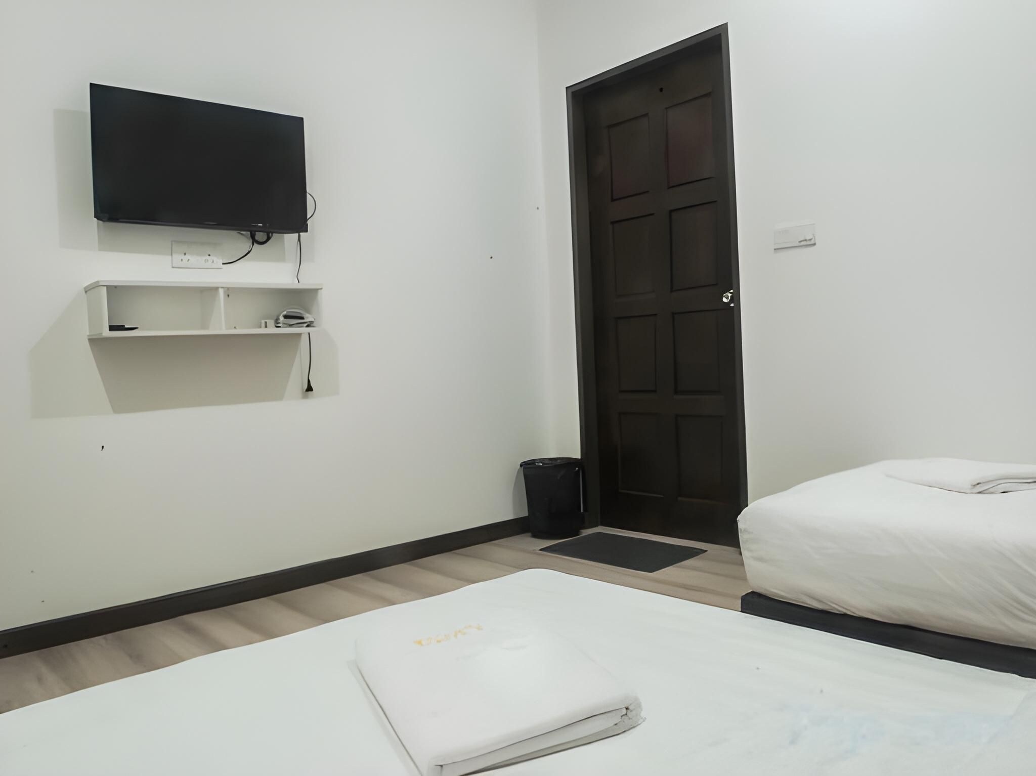 A hotel room with a bed, a TV mounted on the wall, a door, and a small trash bin.