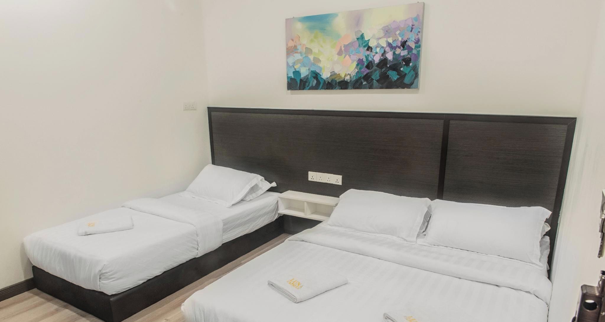 A hotel room with two single beds, a dark headboard, a painting on the wall, and a small bedside table.