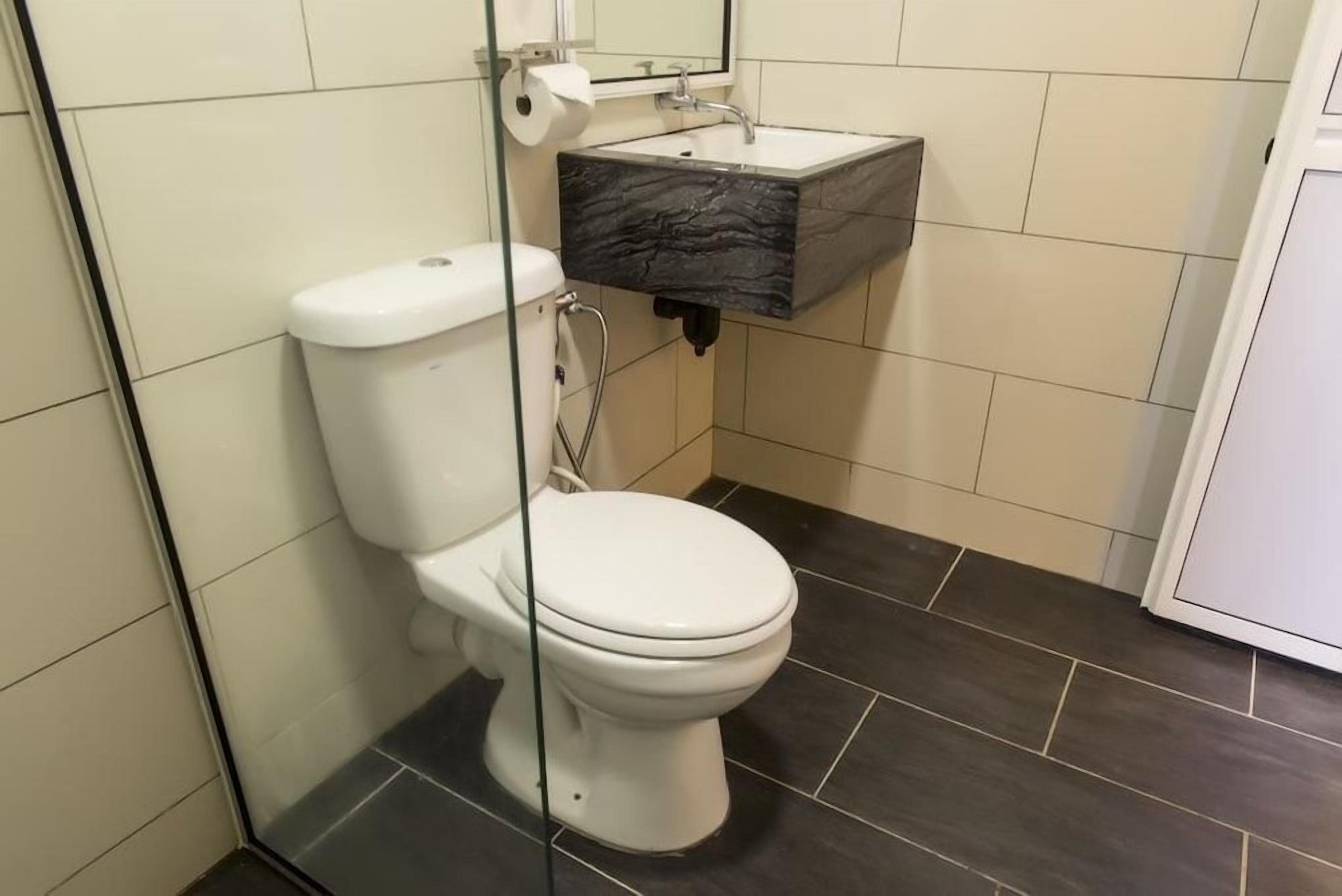 A bathroom with a white toilet, a black marble sink, and dark tiled flooring.