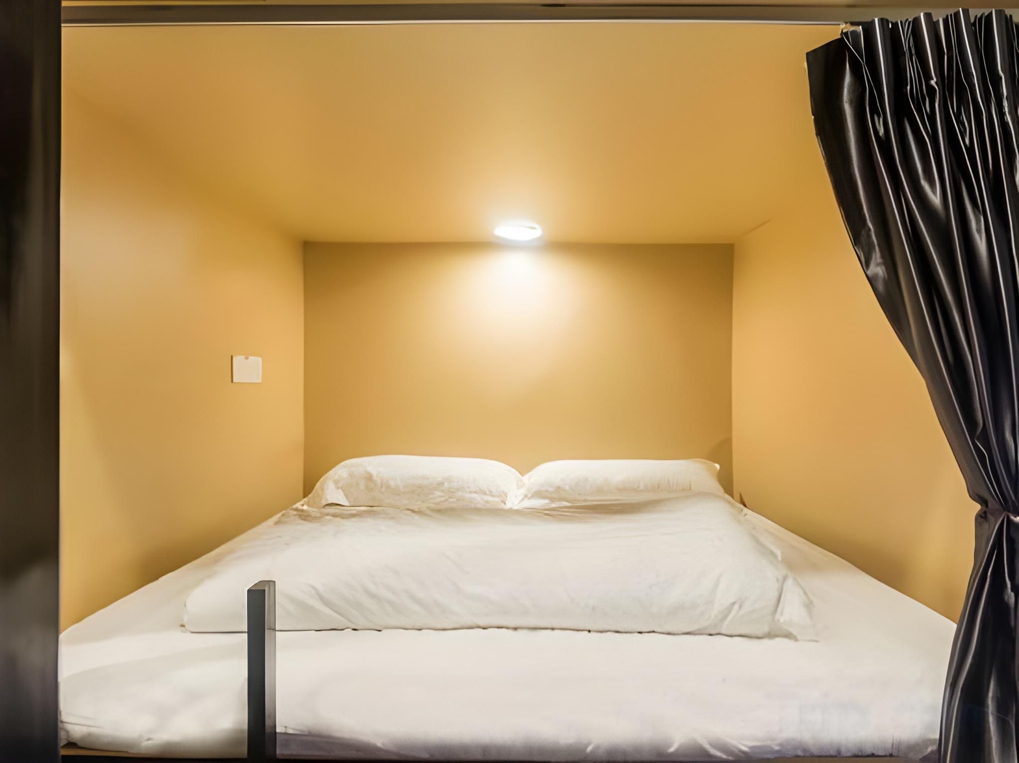 A single bed with white bedding in a room with yellow walls and a ceiling light.