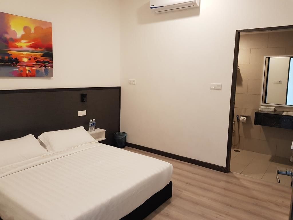 A hotel room with a bed, bedside table, and a painting of a sunset.