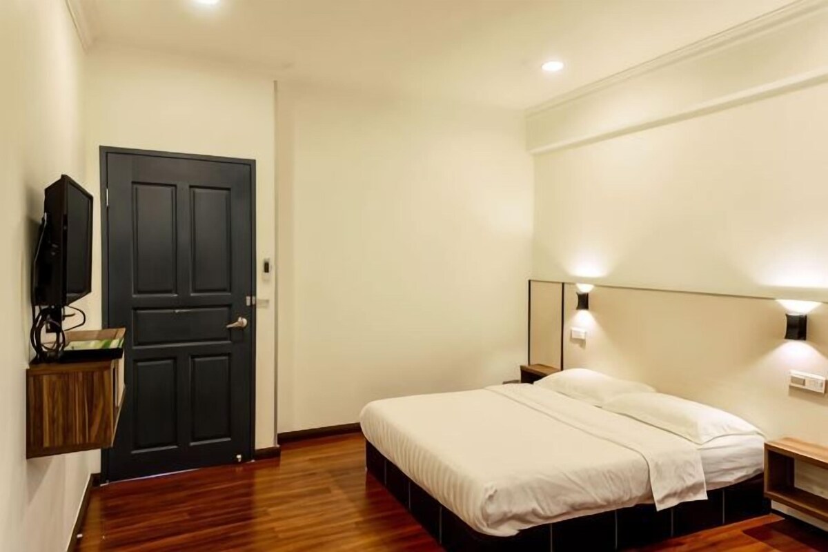 A bedroom with a bed, bedside table, wall-mounted TV, and a door.