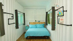 Habitación pequeña con cama individual, diseño de pared a rayas, suelo de madera y ventana con cortinas.