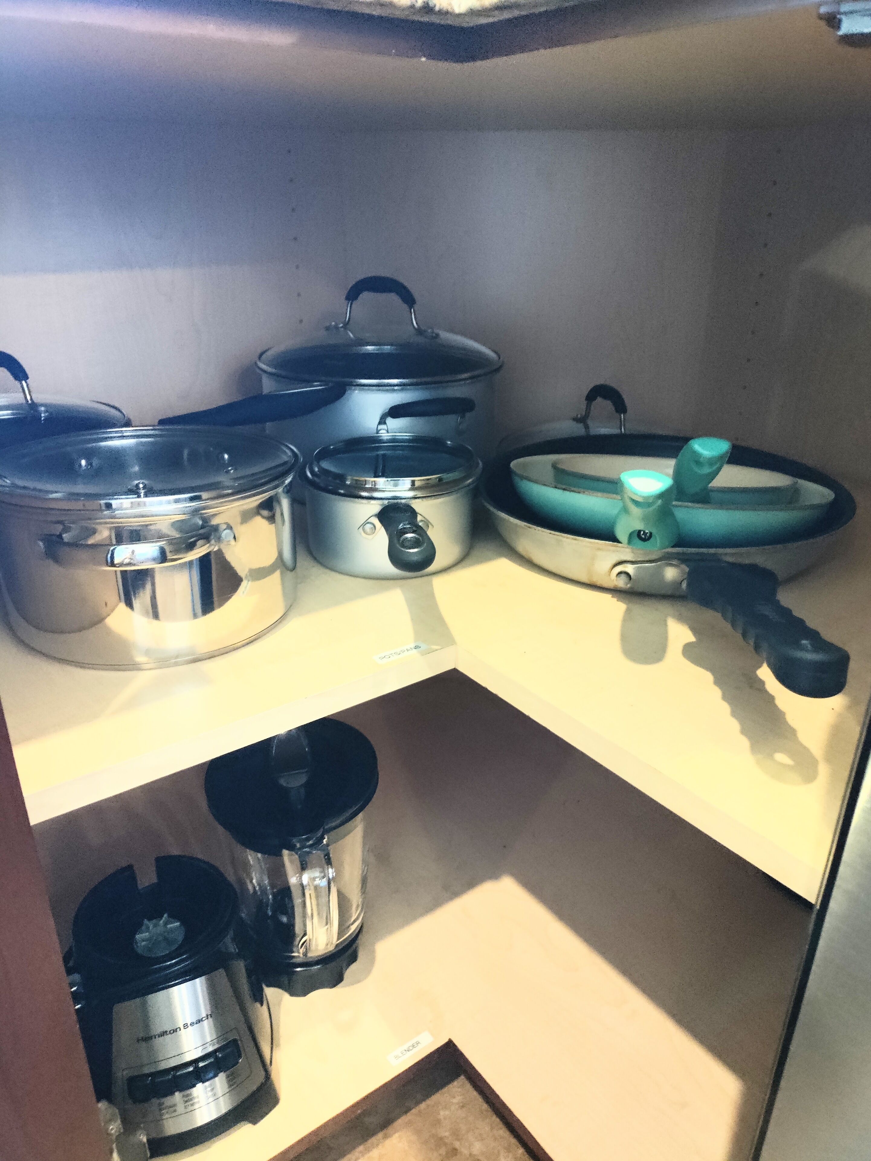 A kitchen with stainless steel pots and pans on shelves, a blender, and a coffee maker.