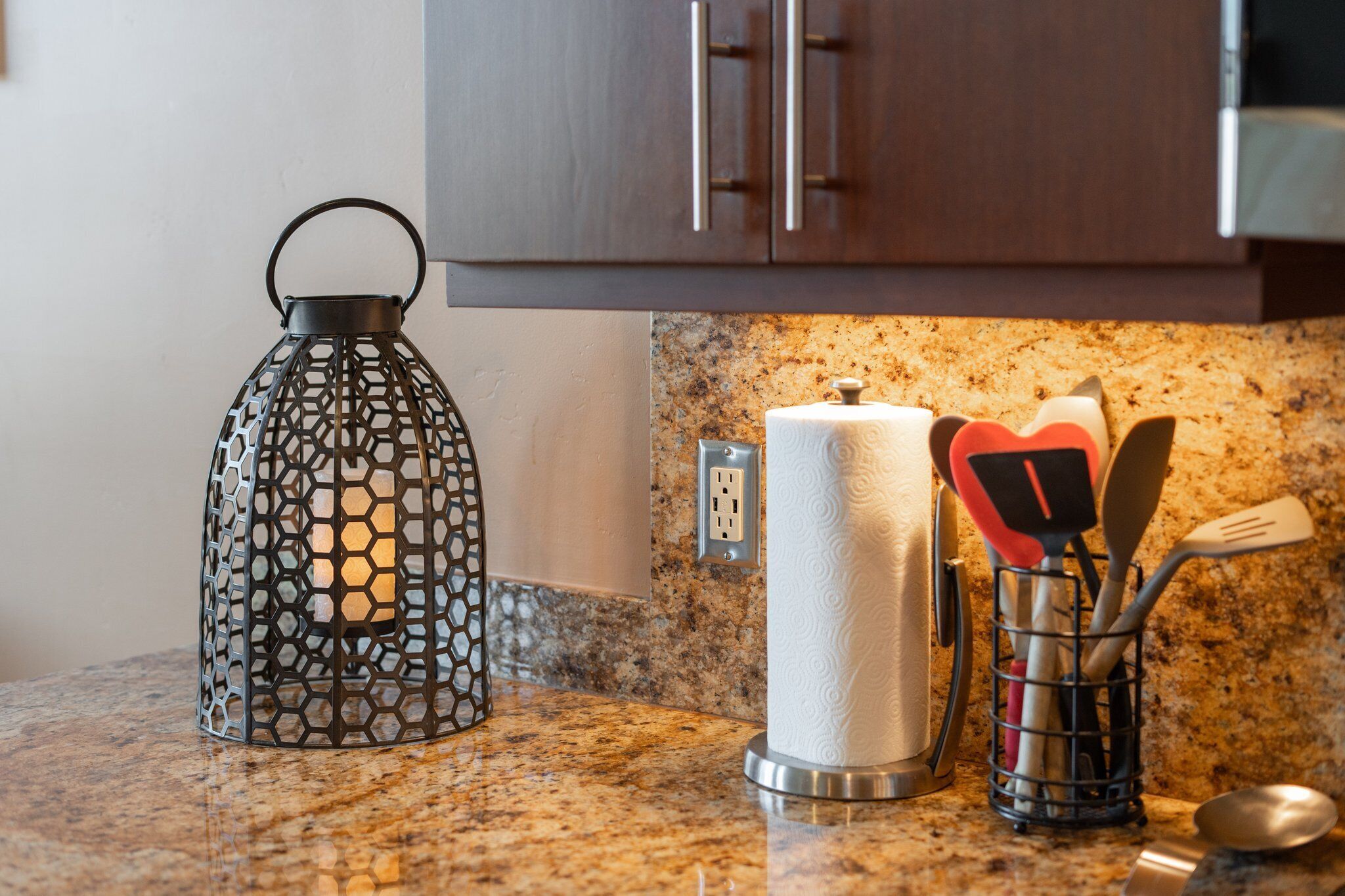 A kitchen counter with a metal lantern, a roll of paper towels, and a utensil holder.