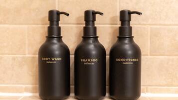 Three black bottles of body wash, shampoo, and conditioner on a tiled surface.