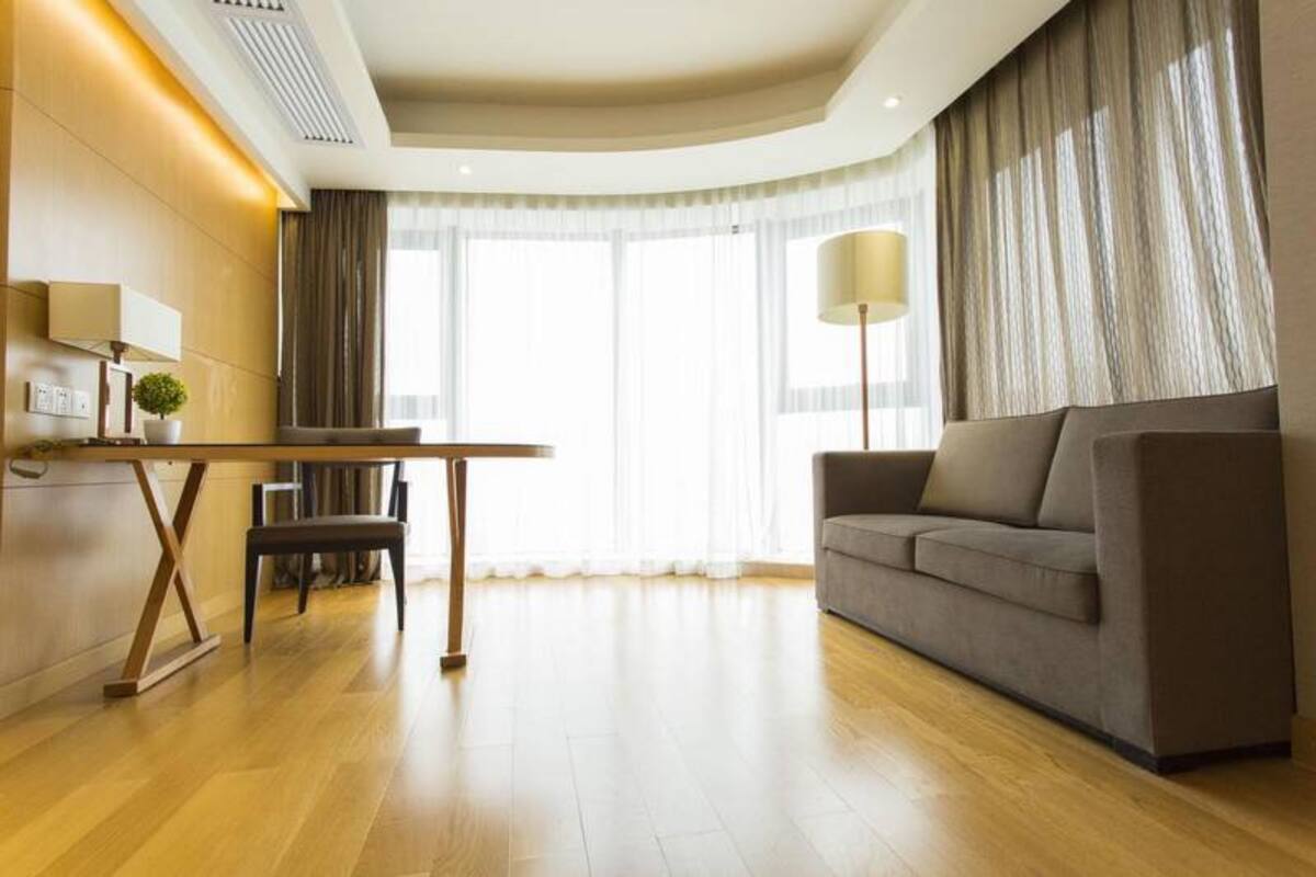 Una habitación de hotel moderna con suelo de madera, un sofá, una mesa de comedor y una lámpara.