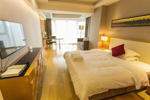 Ein Hotelzimmer mit einem großen Bett, einem Schreibtisch mit Fernseher, einem Sessel und einer Couch.