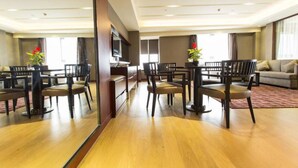 A hotel dining area with wooden flooring, a central dining table with chairs, a sofa, and a TV mounted on the wall. - Guangzhou Yiyuan Apartment (Guangzhou)