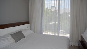 A hotel room with a bed, a bedside table, a lamp, and a window with sheer curtains. - MOMA Luxury condo Playa del Carmen (Playa del Carmen)