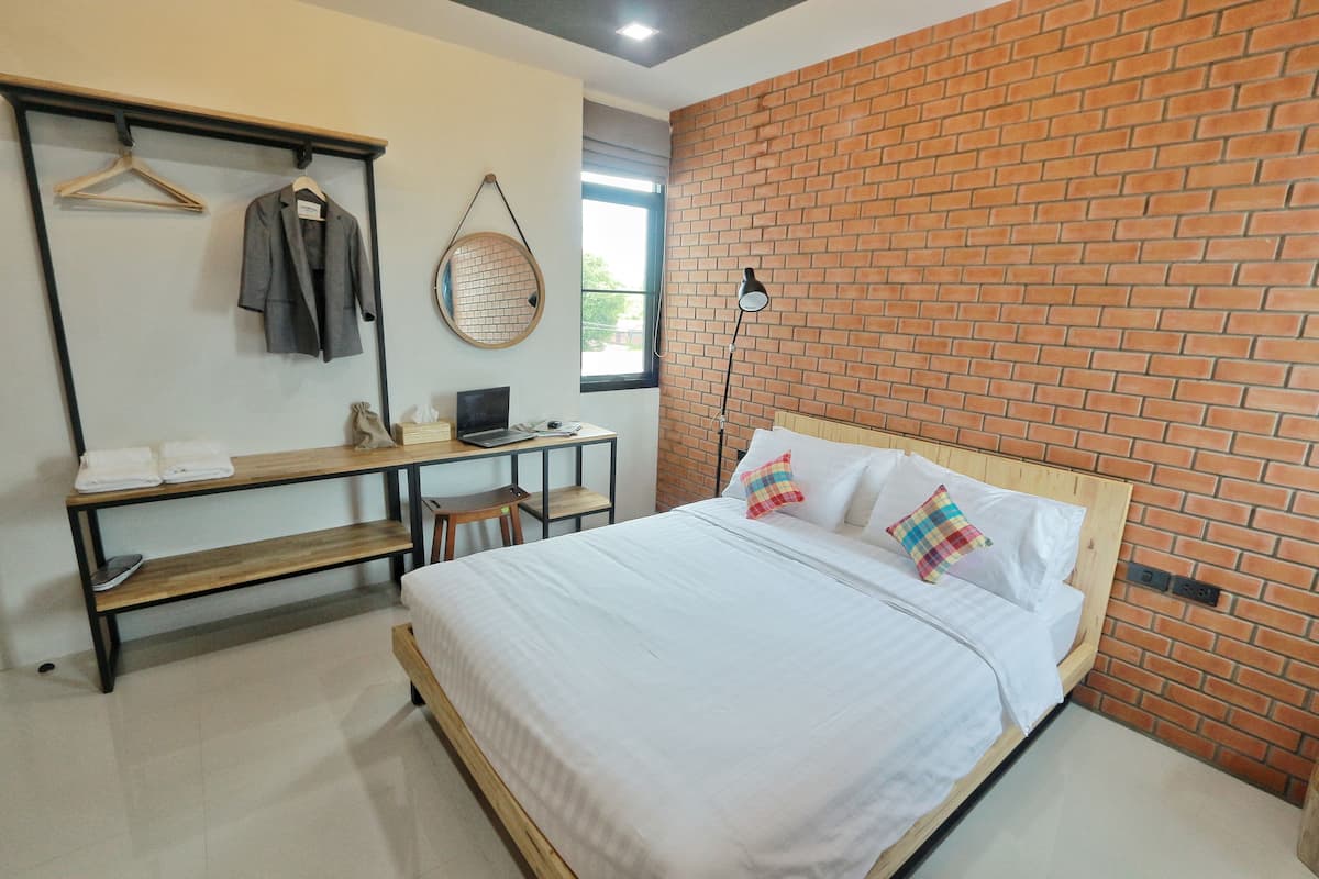 A bedroom with a bed, a desk, a chair, a hanging coat rack, and a window.