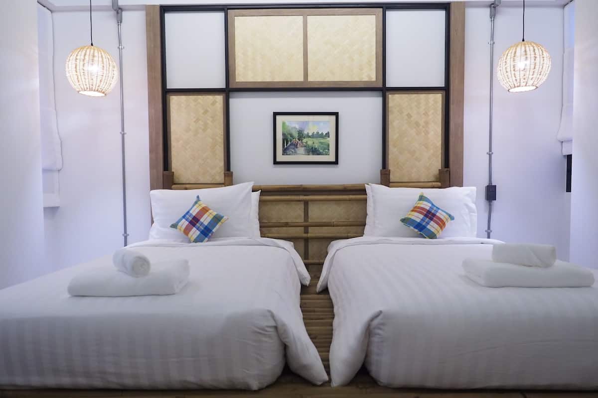 A hotel room with two beds, a wooden headboard, a framed picture on the wall, and two hanging light fixtures.