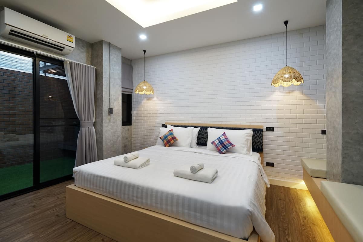 A modern bedroom with a large bed, two bedside tables, a ceiling light, and a sliding glass door to the left.