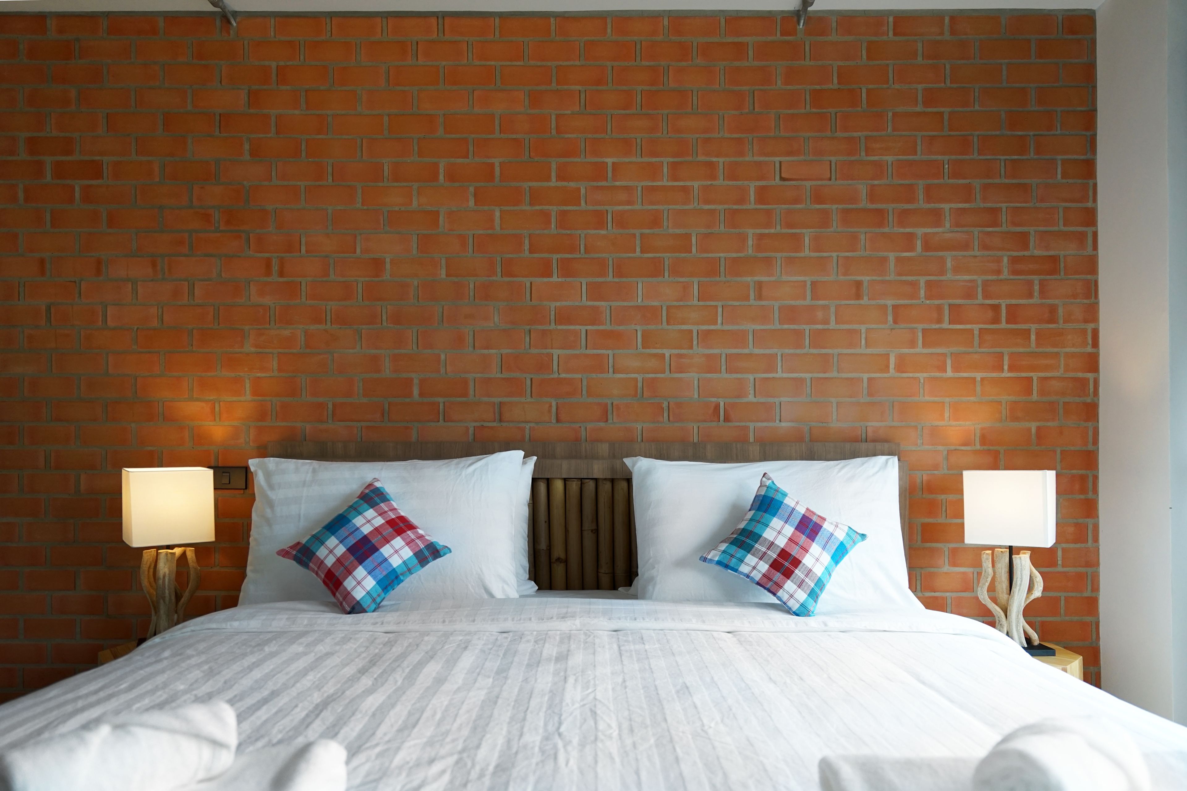 Een hotelkamer met een hoofdbord van baksteenmotief, wit beddengoed en twee bedlampjes.