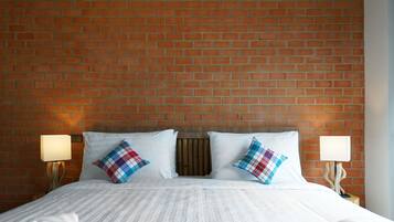 Een hotelkamer met een hoofdbord van baksteenmotief, wit beddengoed en twee bedlampjes.