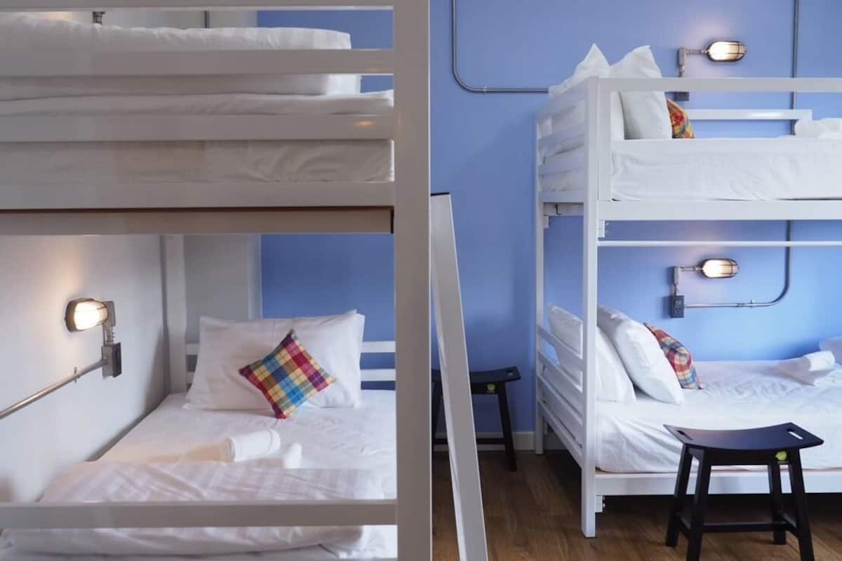 A bunk bed room with two beds, each with a bedside table and lamp.