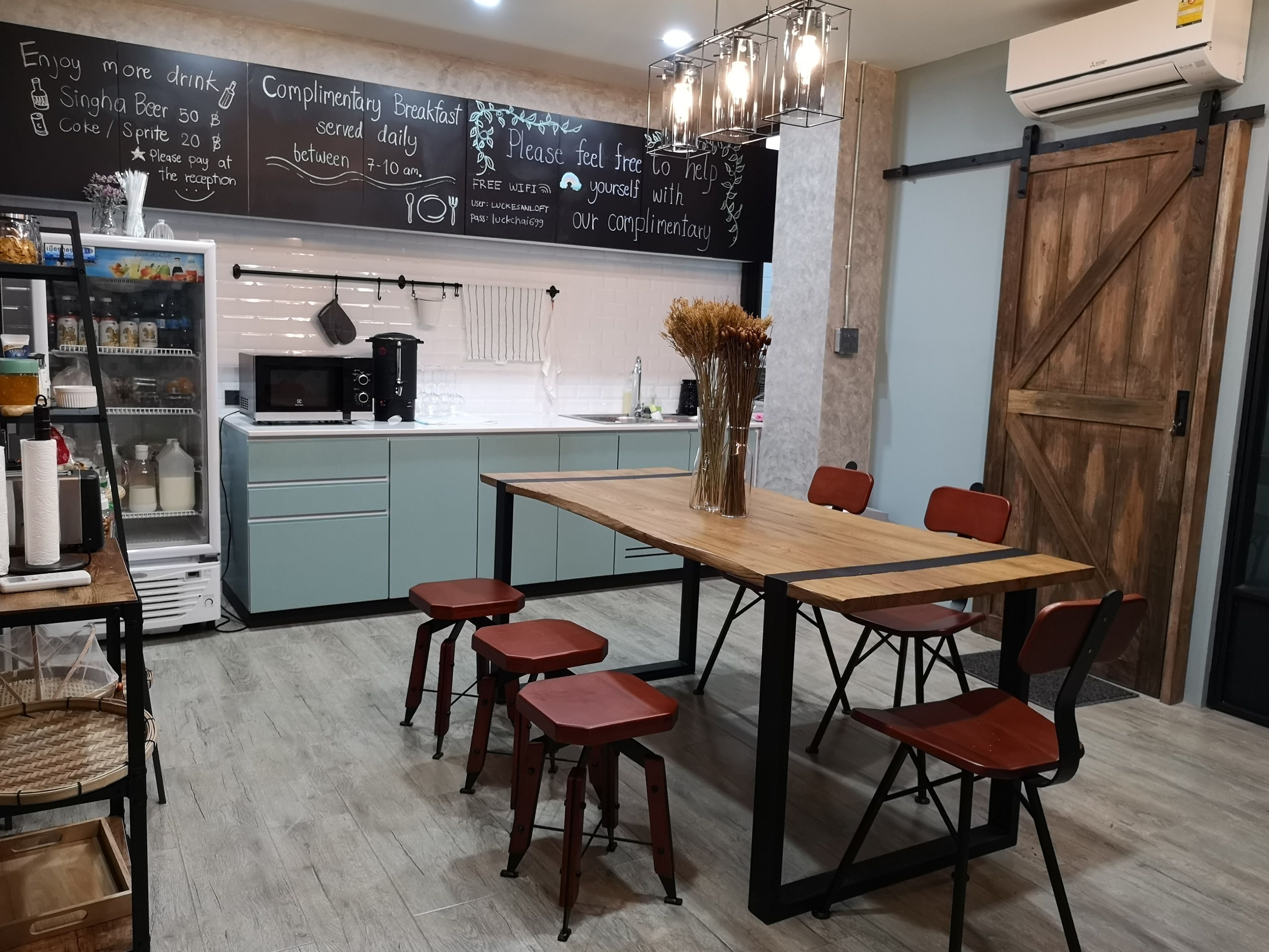 A modern kitchen with a chalkboard menu, a wooden dining table with chairs, and a refrigerator.