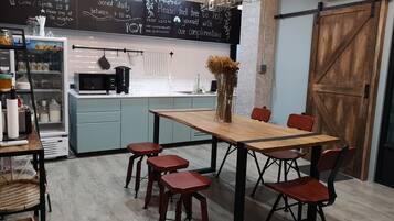 A modern kitchen with a chalkboard menu, a wooden dining table with chairs, and a refrigerator.