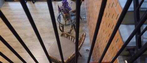 Een modern interieur met een houten trap, een glazen tafel met paarse bloemen, rieten stoelen en een bakstenen muur.