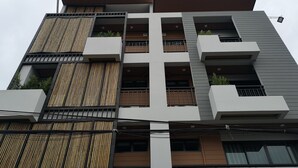A multi-story building with a modern architectural design, featuring balconies, large windows, and a mix of wooden and metal elements. - Luck Esan Loft - Hostel (Ubon Ratchathani)
