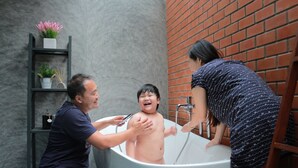 A bathtub with a child and two adults, one adult is holding a showerhead. - Luck Esan Loft - Hostel (Ubon Ratchathani)
