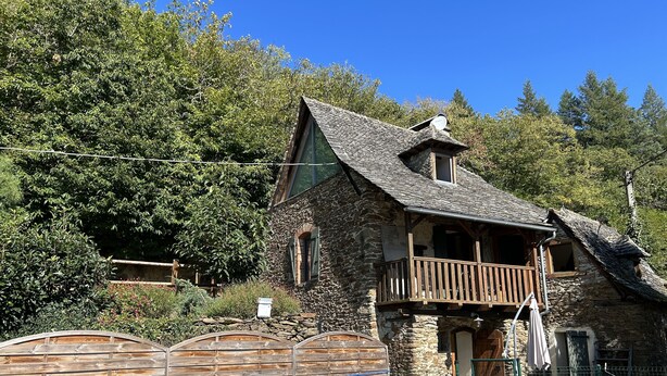 Um edifício de pedra com varanda, rodeado por árvores.