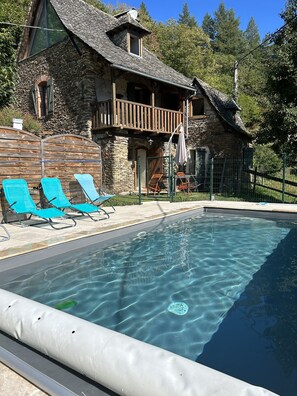 Ein Gebäude aus Stein mit Schwimmbecken, Holzterrasse und Liegestühlen.