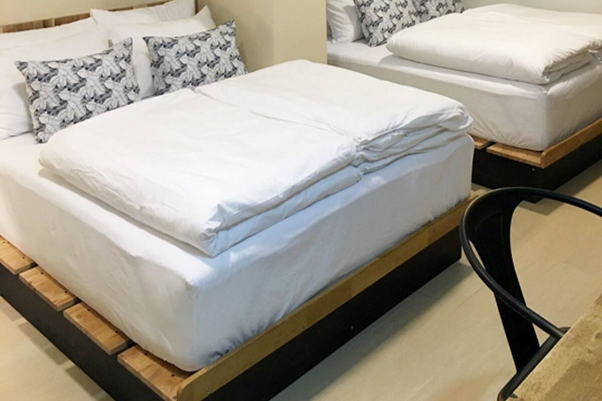 A hotel room with two beds, each with white bedding and patterned pillows. There is a wall decoration above the beds and a ceiling light.