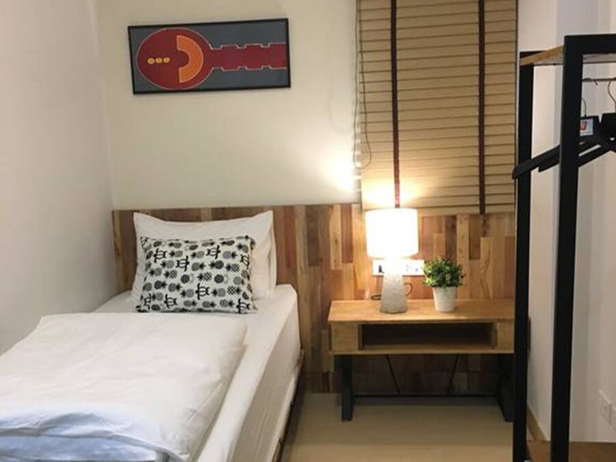 Habitació petita i ben ordenada amb llit, taulell de nit, làmpada i aparell d'aire condicionat.